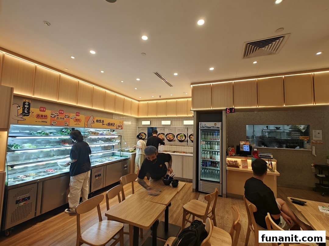 Bright interior of Gong Yuan Mala Tang, featuring a fresh ingredient bar, dining area, and staff.