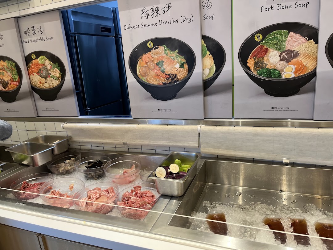 A self-service counter displaying fresh ingredients for customizable hotpot, with illustrative dish posters above.