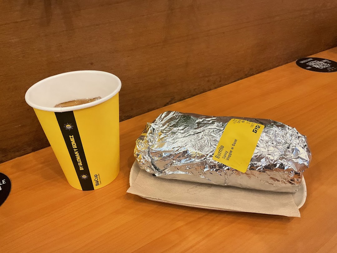 A foil-wrapped Spicy Veggie Burrito with Guac and a branded drink cup from Guzman y Gomez.