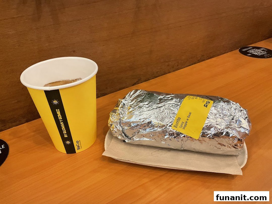 A foil-wrapped Spicy Veggie Burrito with Guac and a branded drink cup from Guzman y Gomez.
