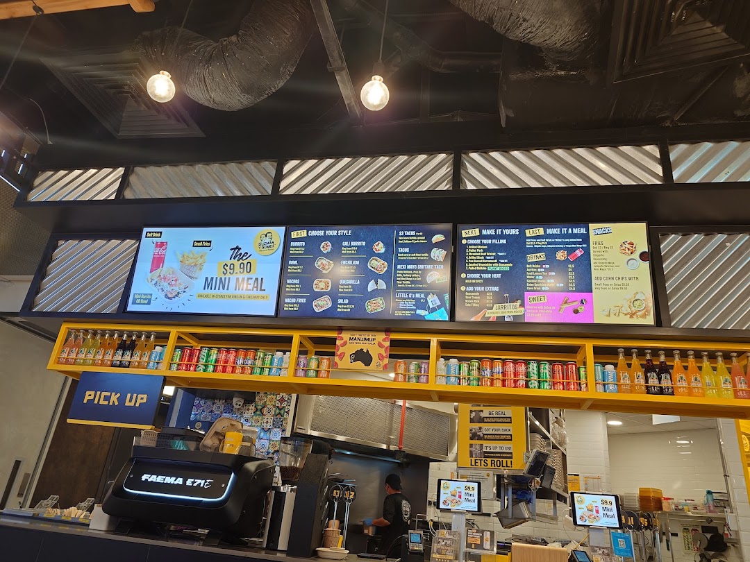 An interior view of Guzman y Gomez, showcasing digital menu boards, the counter, and a glimpse of the kitchen.