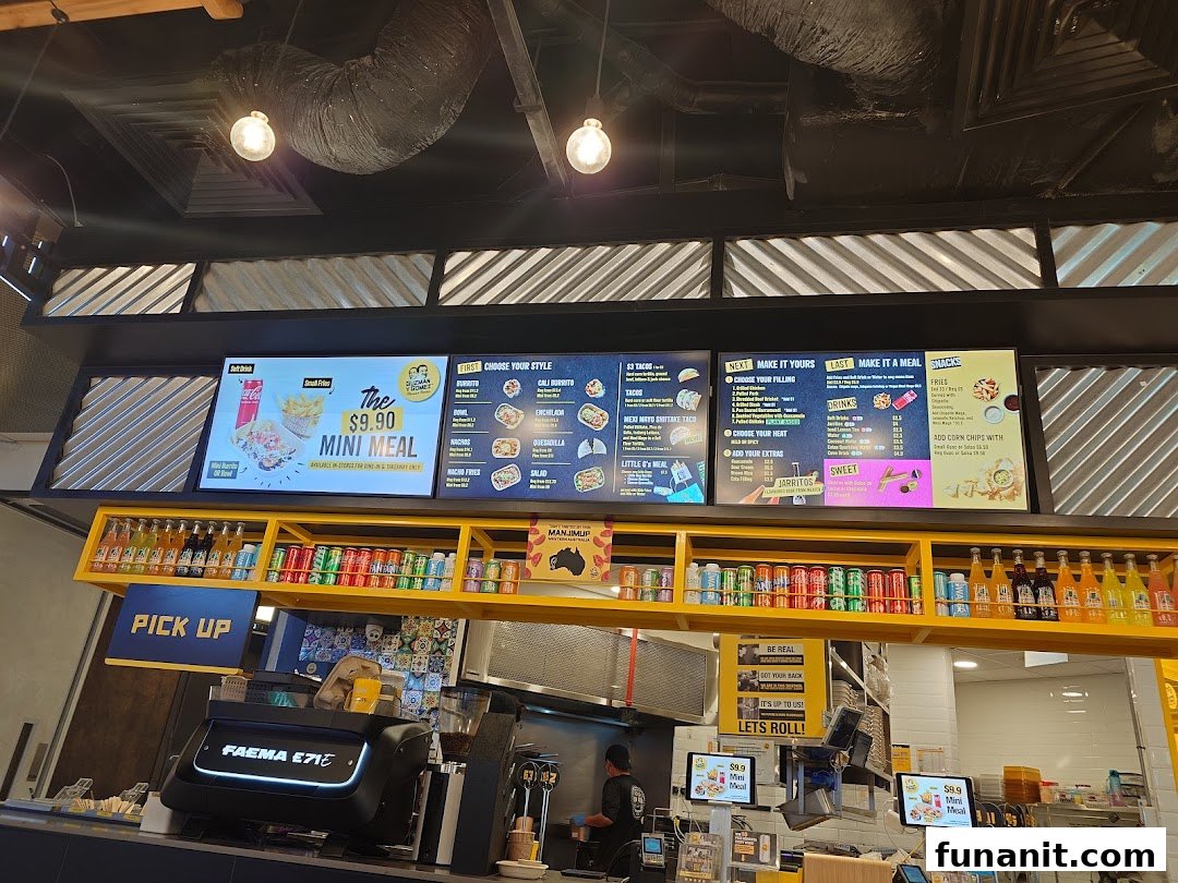 An interior view of Guzman y Gomez, showcasing digital menu boards, the counter, and a glimpse of the kitchen.