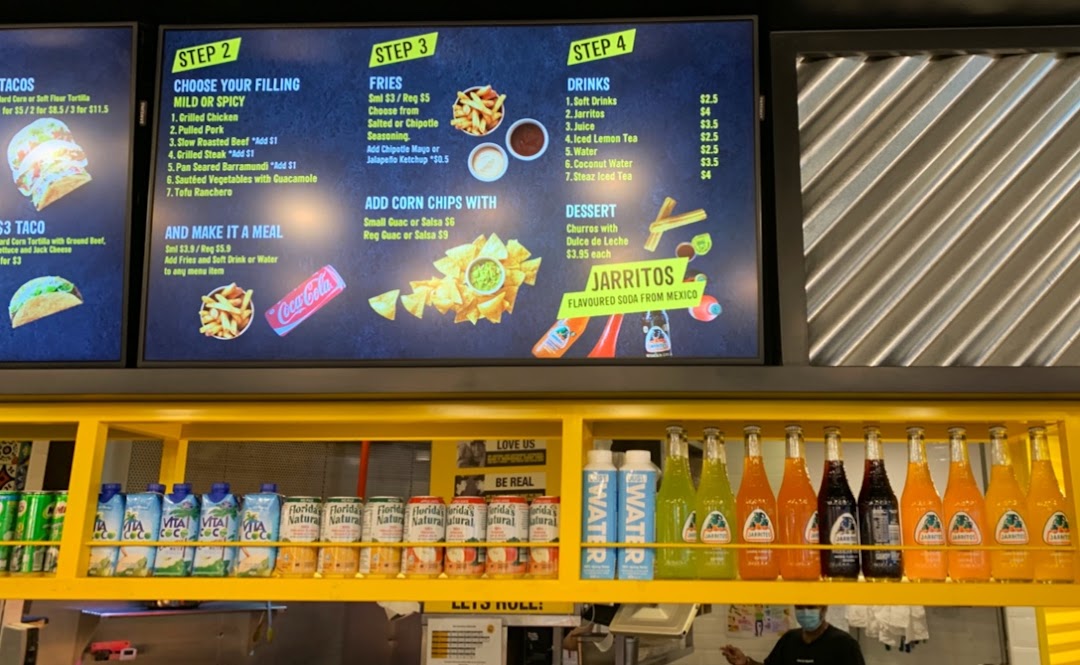 A digital menu board at Guzman y Gomez displaying various Mexican food options, drinks, and prices.