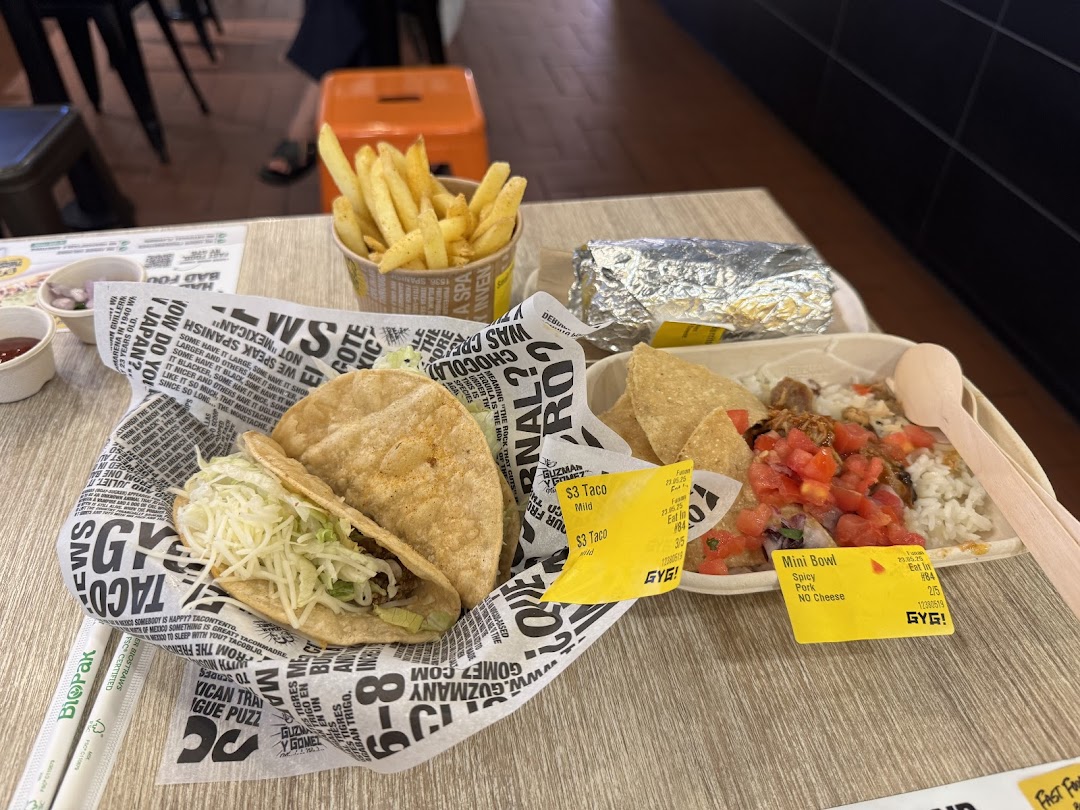 A table spread with Guzman y Gomez Mexican food, including tacos, fries, a burrito, and a mini bowl.