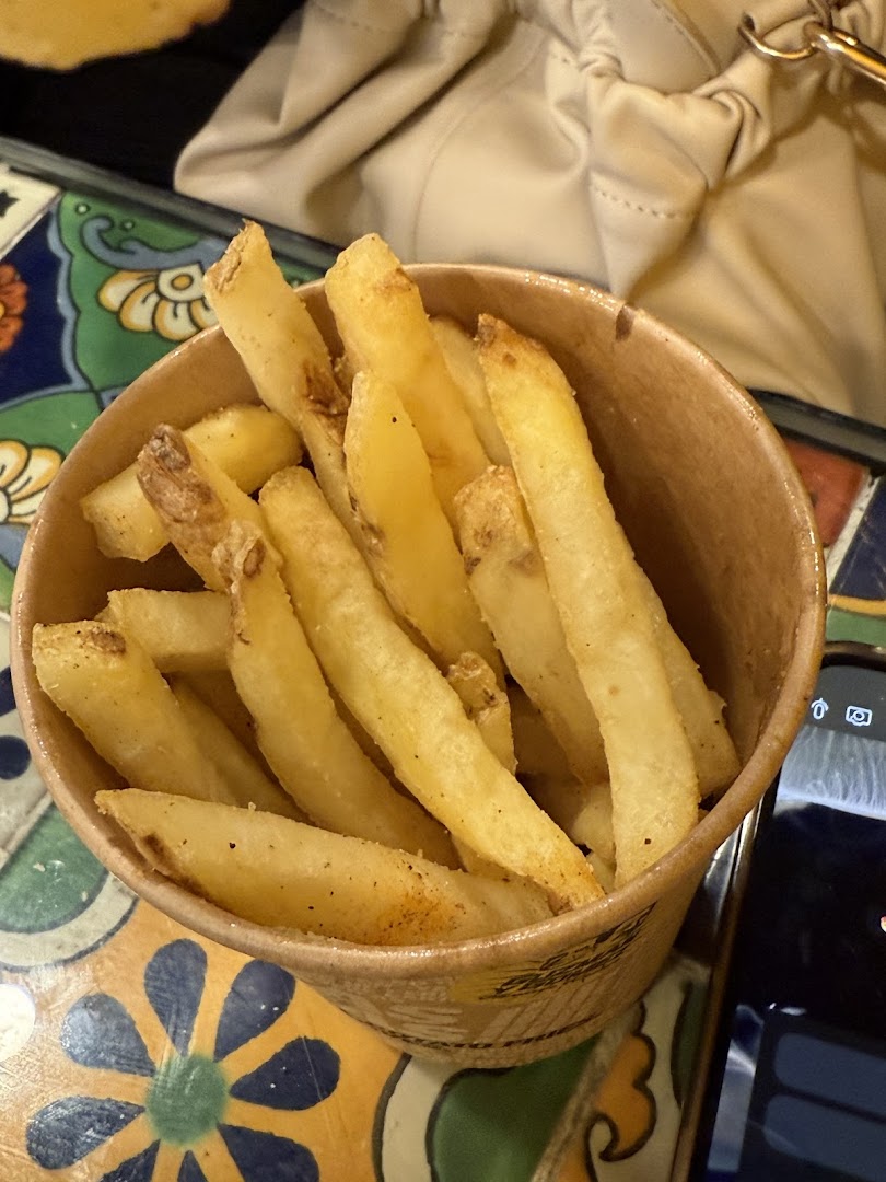 A close-up shot of a cup filled with golden, seasoned french fries from Guzman y Gomez.