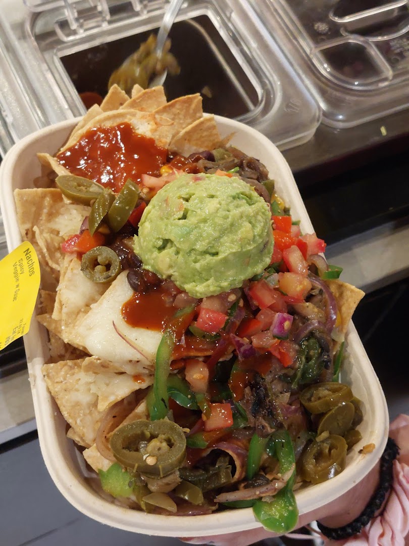 A vibrant bowl of Guzman y Gomez nachos topped with guacamole, salsa, jalapeños, and fresh vegetables.