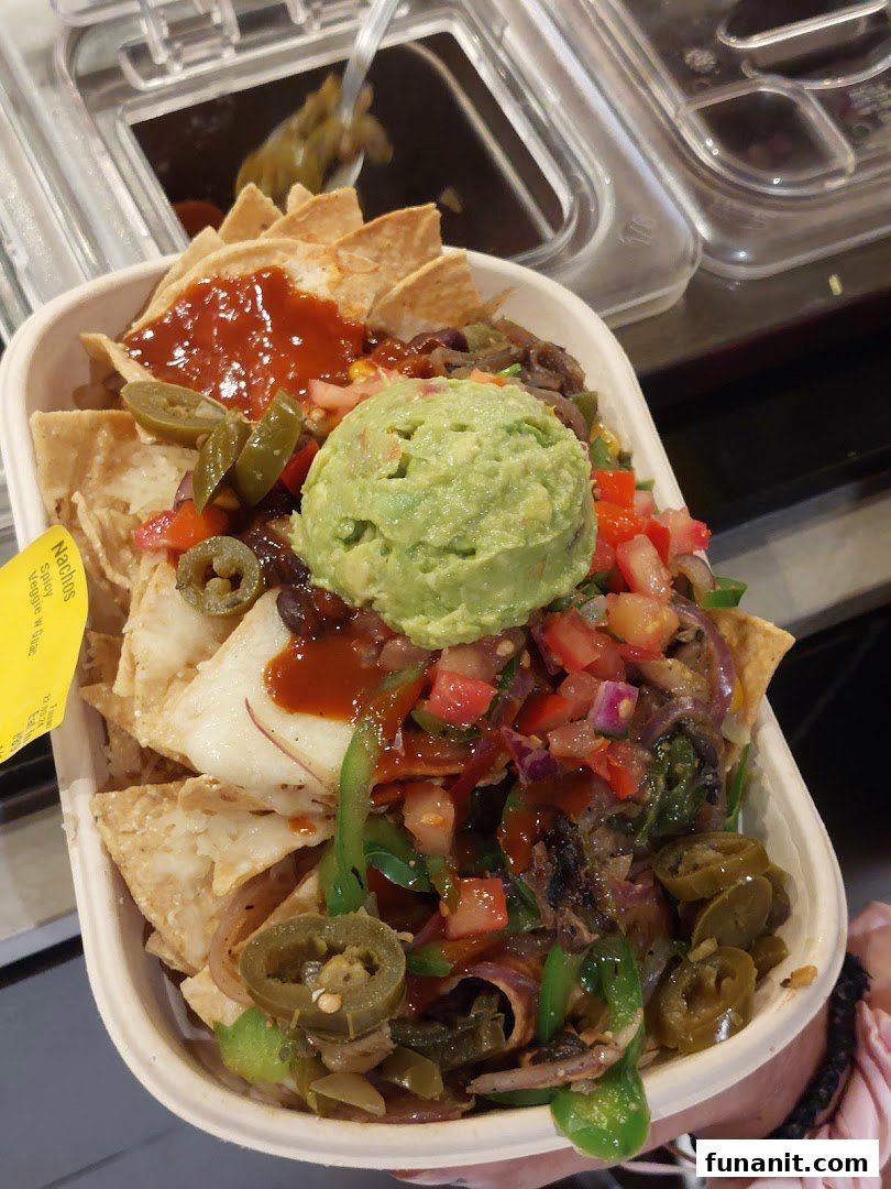 A vibrant bowl of Guzman y Gomez nachos topped with guacamole, salsa, jalapeños, and fresh vegetables.