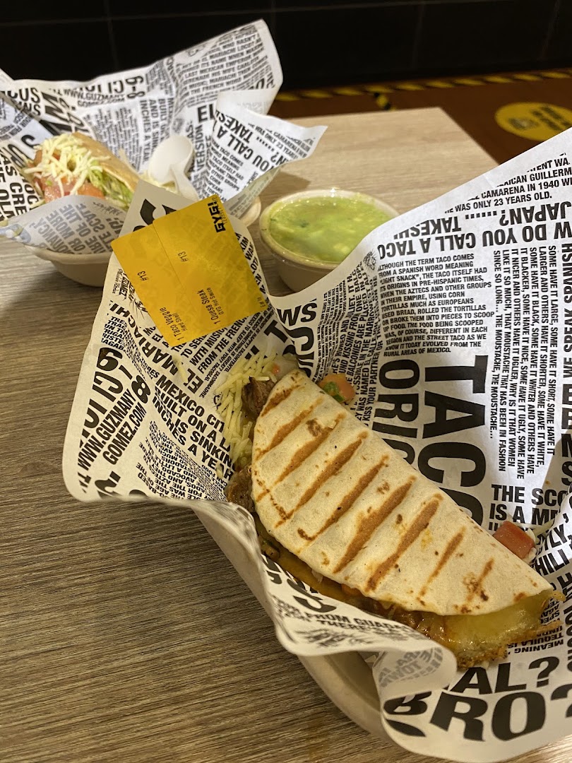 Two delicious Guzman y Gomez tacos/quesadillas with a side of guacamole on a wooden table.