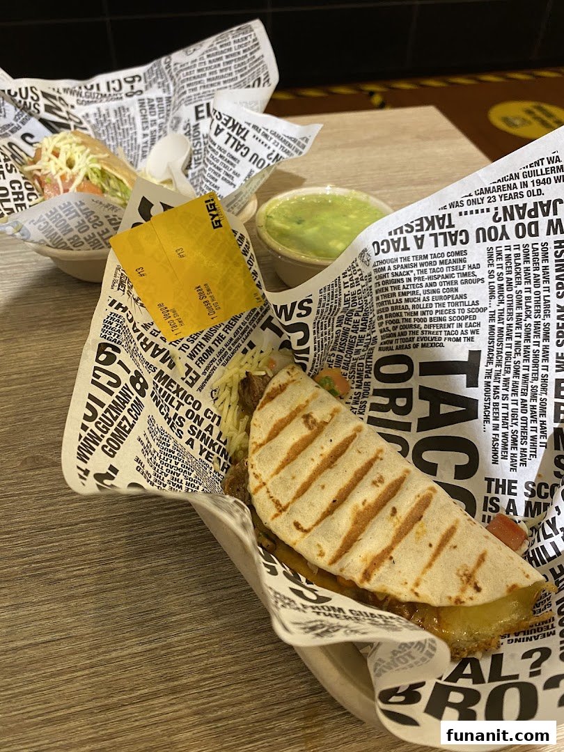 Two delicious Guzman y Gomez tacos/quesadillas with a side of guacamole on a wooden table.
