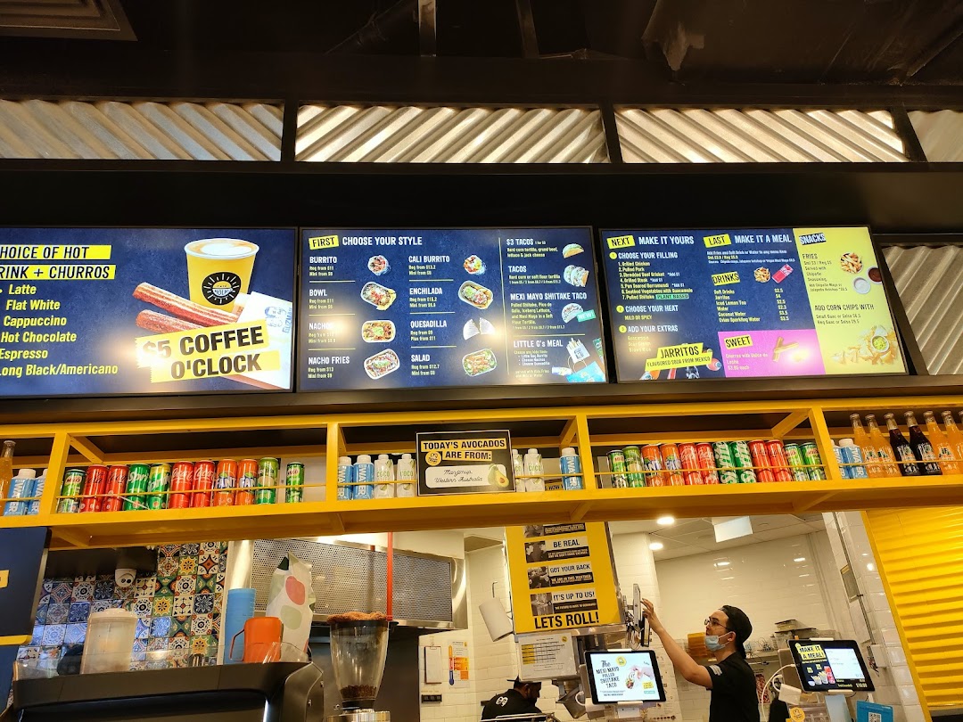 Digital menu boards displaying food and drink options at Guzman y Gomez, with a counter and staff.