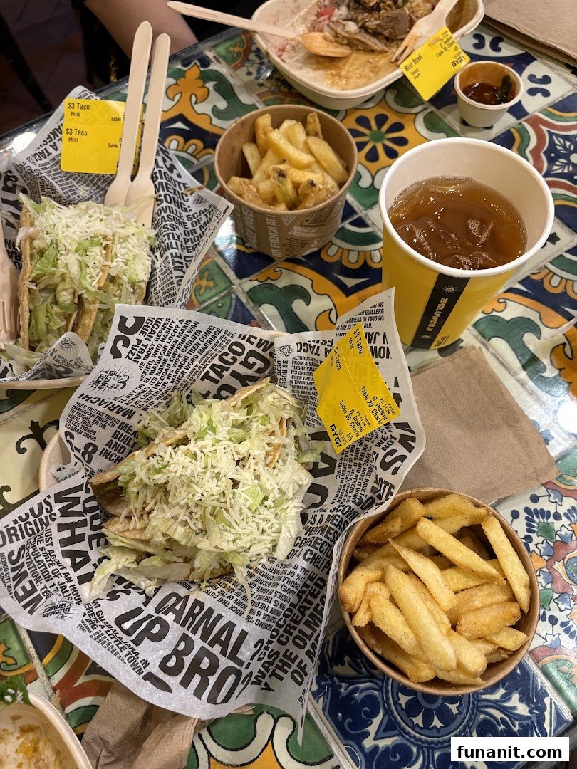 A vibrant close-up of delicious tacos, fries, and a drink from Guzman y Gomez on a colorful tiled table.