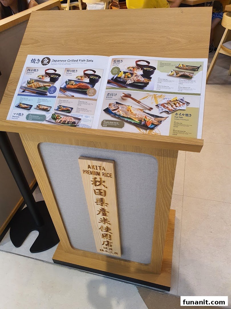 A menu stand showcasing various Japanese grilled fish sets with different cooking styles and prices.