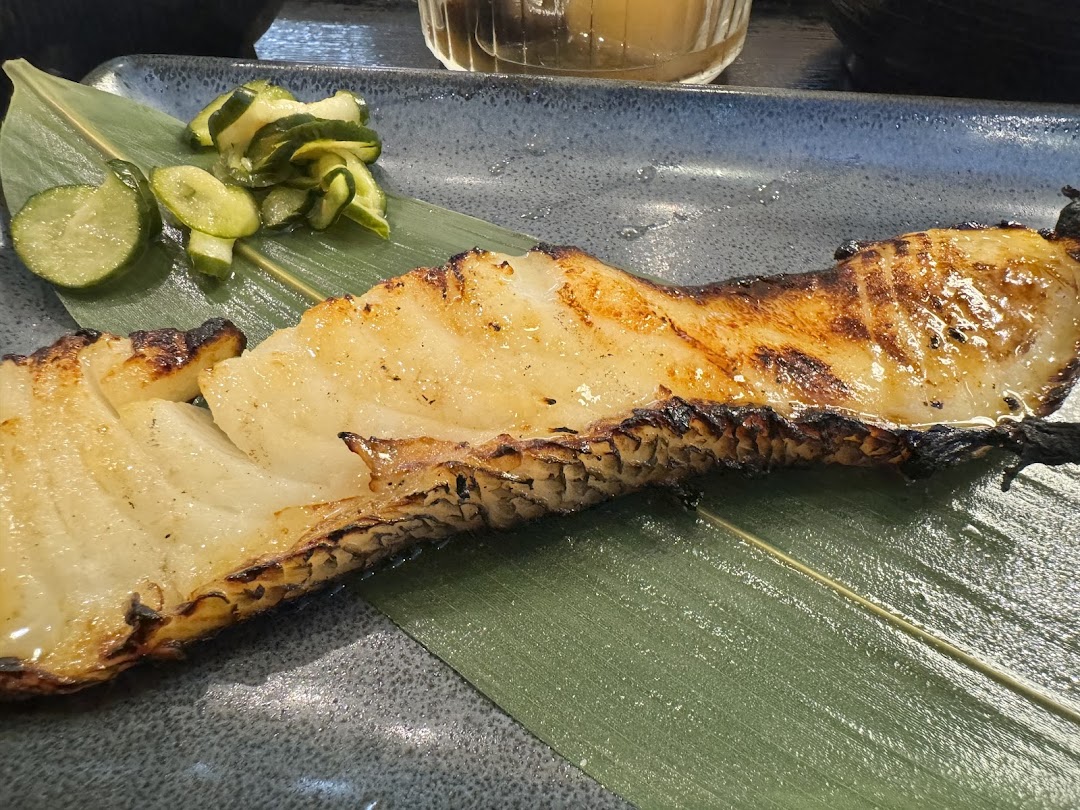 A perfectly grilled fish fillet served on a banana leaf with a side of pickled cucumber slices.