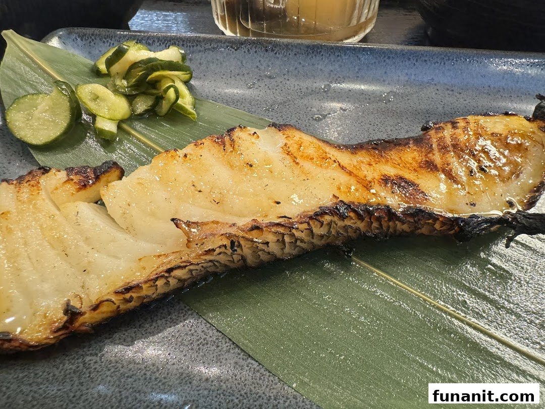 A perfectly grilled fish fillet served on a banana leaf with a side of pickled cucumber slices.