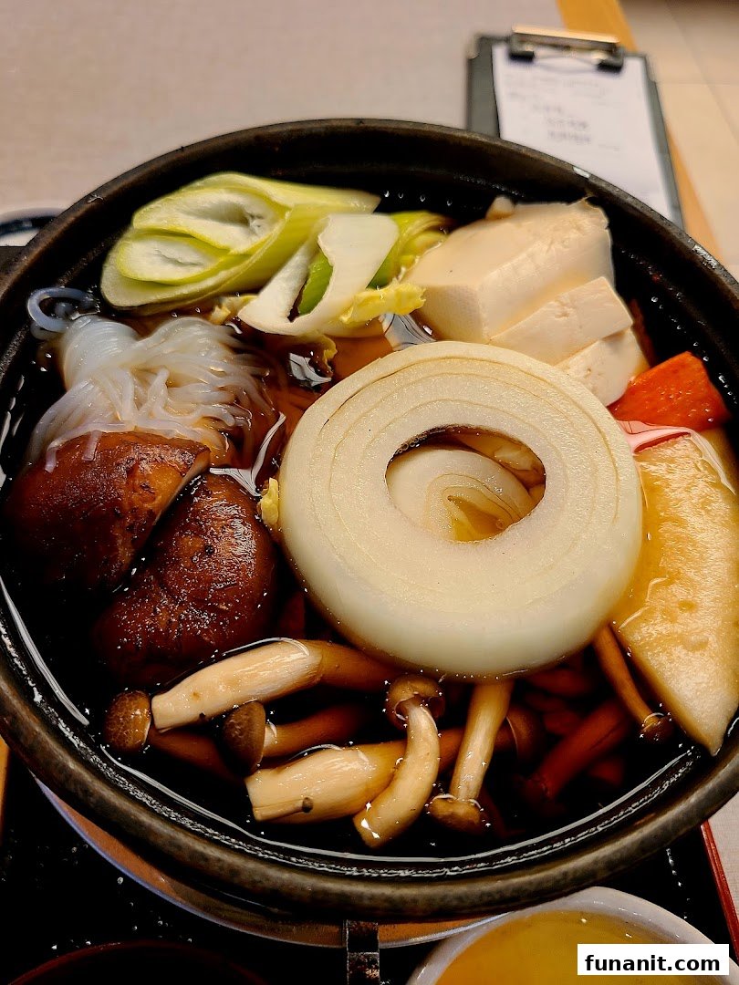 A close-up of a delicious Japanese sukiyaki pot filled with fresh vegetables, mushrooms, tofu, and noodles.