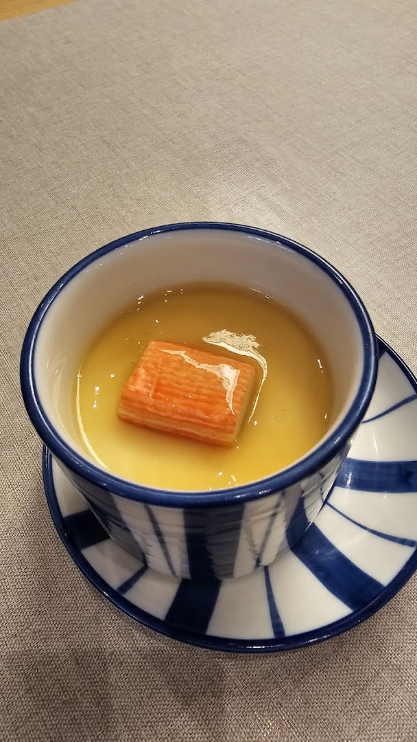 A close-up of a Japanese chawanmushi (steamed egg custard) with a crab stick, served in a blue and white bowl.