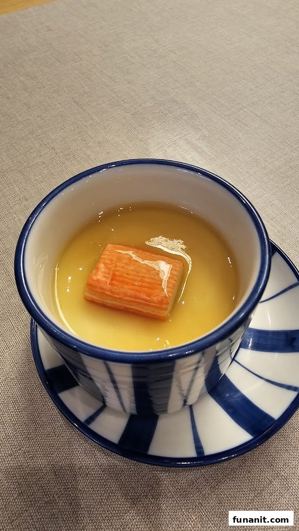A close-up of a Japanese chawanmushi (steamed egg custard) with a crab stick, served in a blue and white bowl.