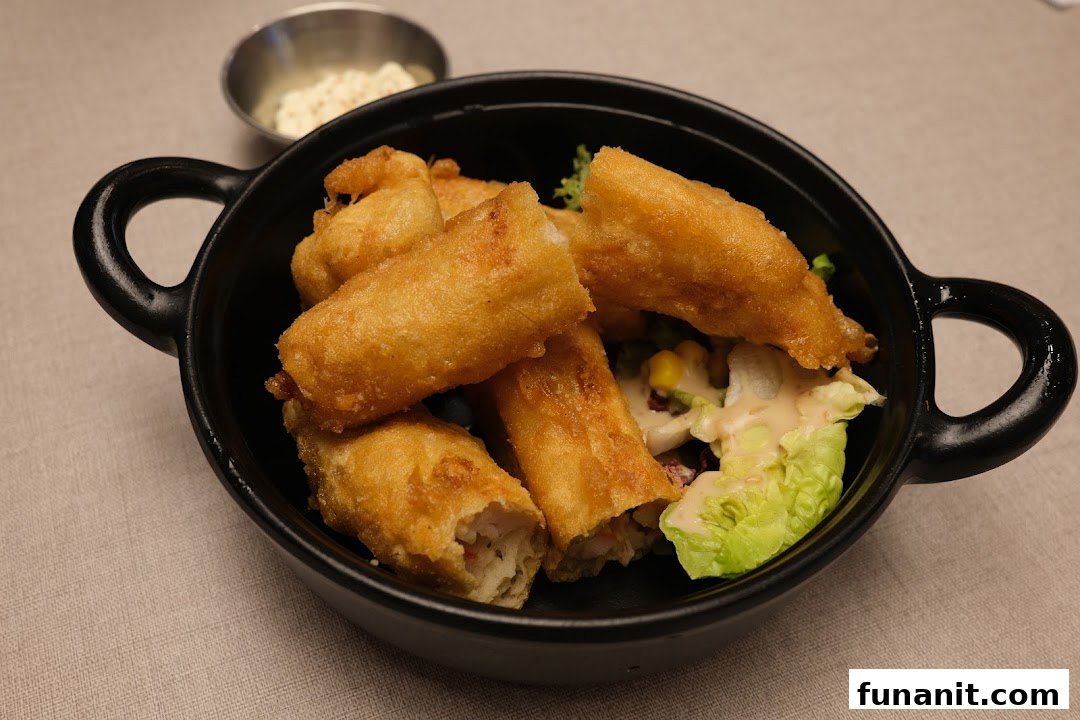 A close-up of golden-fried fish rolls or spring rolls served with a fresh salad and dipping sauce.