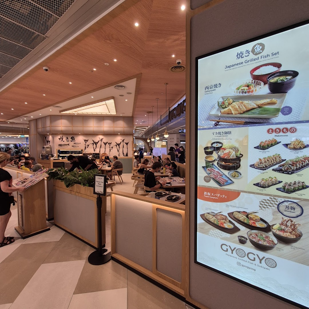 A vibrant interior shot of GyoGyo Japanese restaurant with diners and a prominent digital menu display.