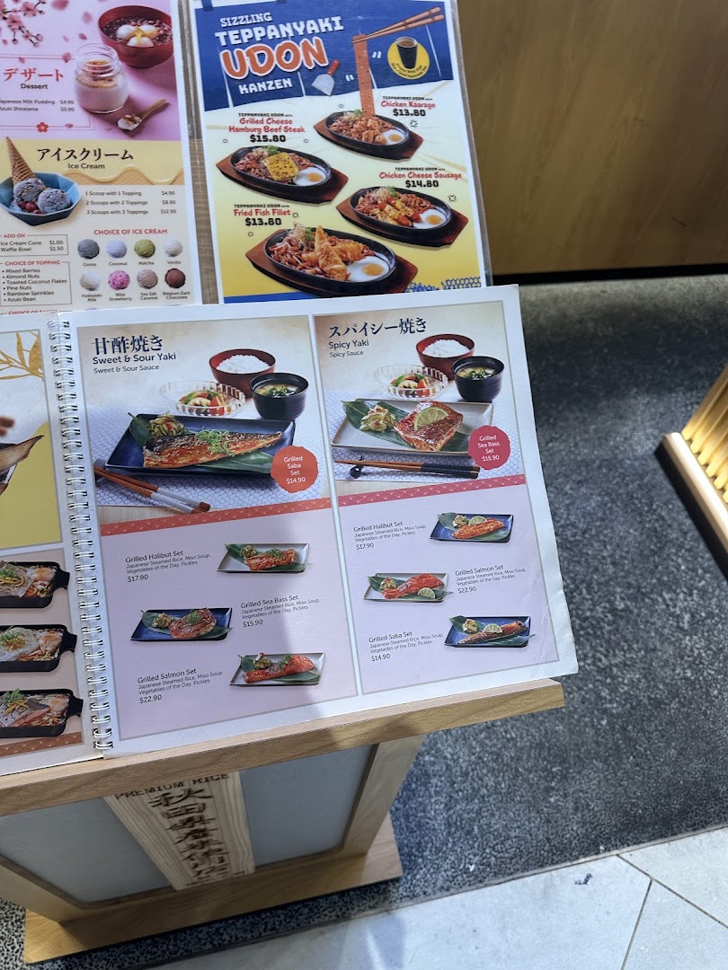 A detailed menu stand showcasing various Japanese grilled fish, sukiyaki, teppanyaki udon, and dessert options.