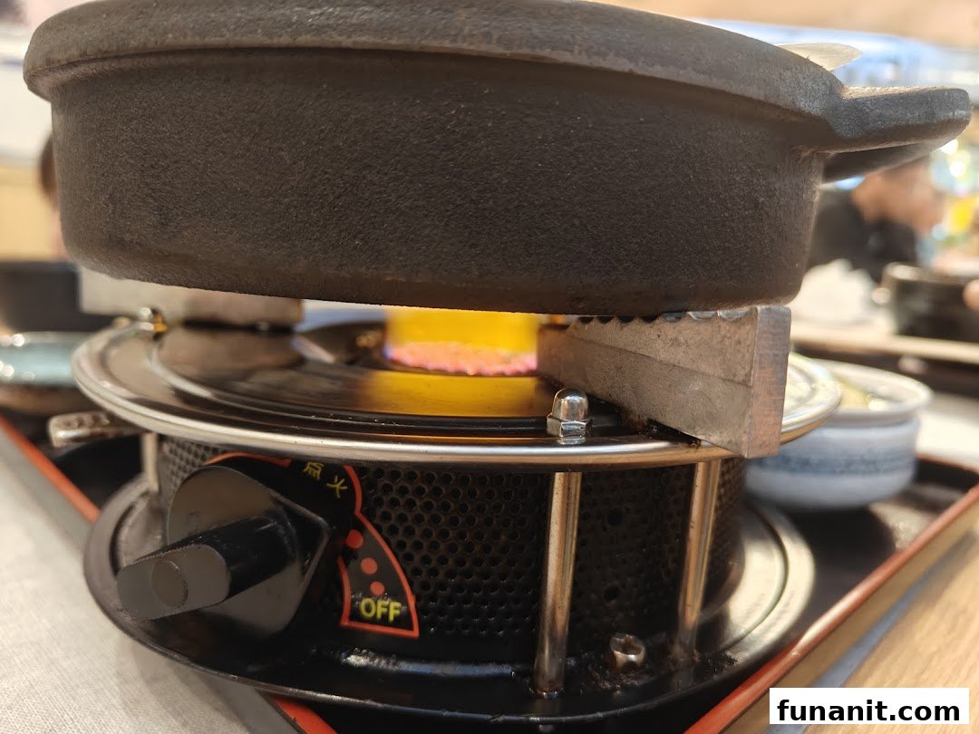 A close-up of a hot pot cooking on a portable burner with a visible flame.