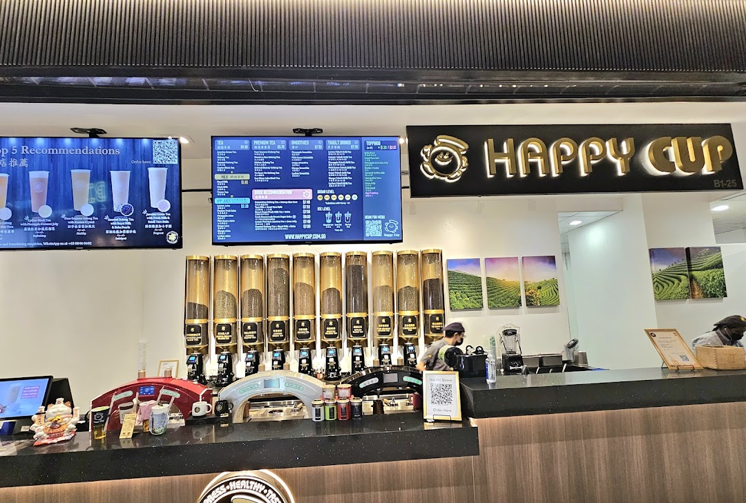 An interior view of Happy Cup Funan, showcasing the counter, tea dispensers, and digital menu boards.