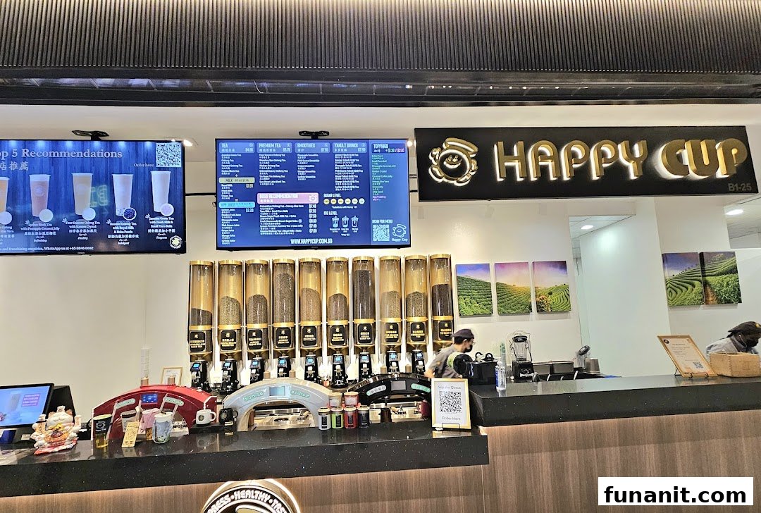 An interior view of Happy Cup Funan, showcasing the counter, tea dispensers, and digital menu boards.