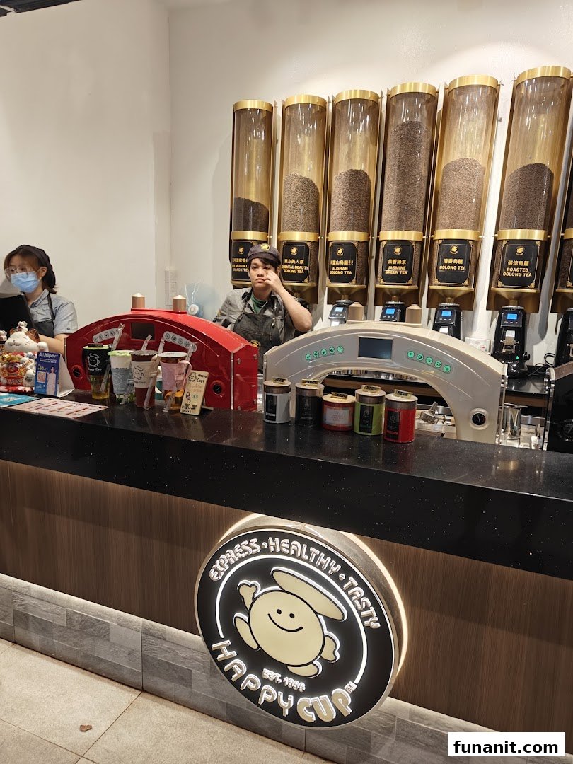 Two staff members at the counter of Happy Cup, with large tea dispensers and brewing equipment visible.