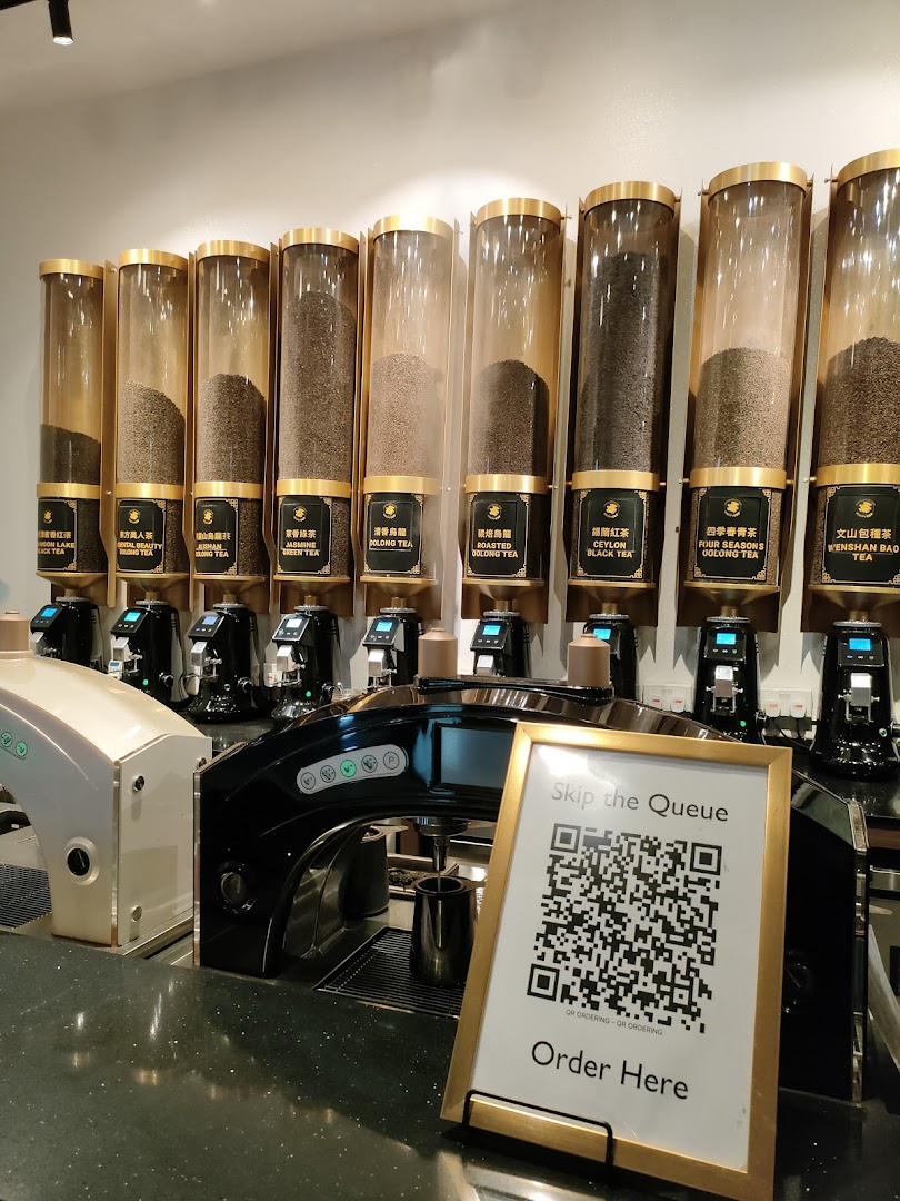 A display of various tea leaves in dispensers with brewing machines and a QR code for ordering.
