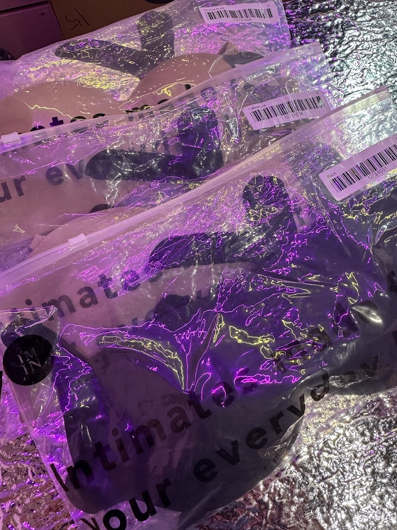 Close-up of packaged intimate apparel from IM IN IMINXX, illuminated by vibrant purple lighting.