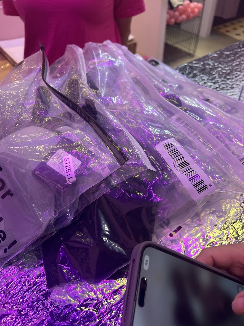 Packaged apparel items with size labels under vibrant purple lighting in a retail setting.
