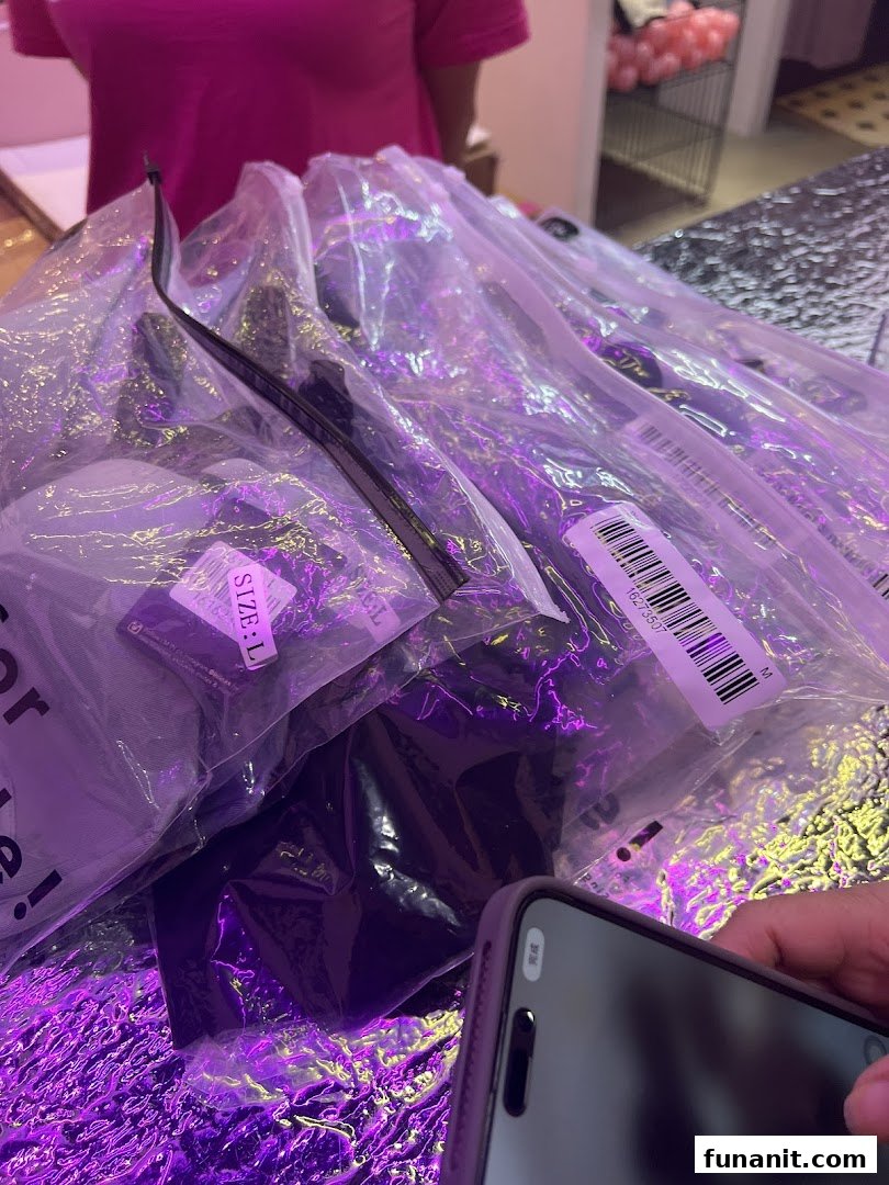 Packaged apparel items with size labels under vibrant purple lighting in a retail setting.