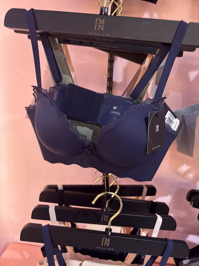 A dark blue bra with lace details displayed on a hanger in a retail store.
