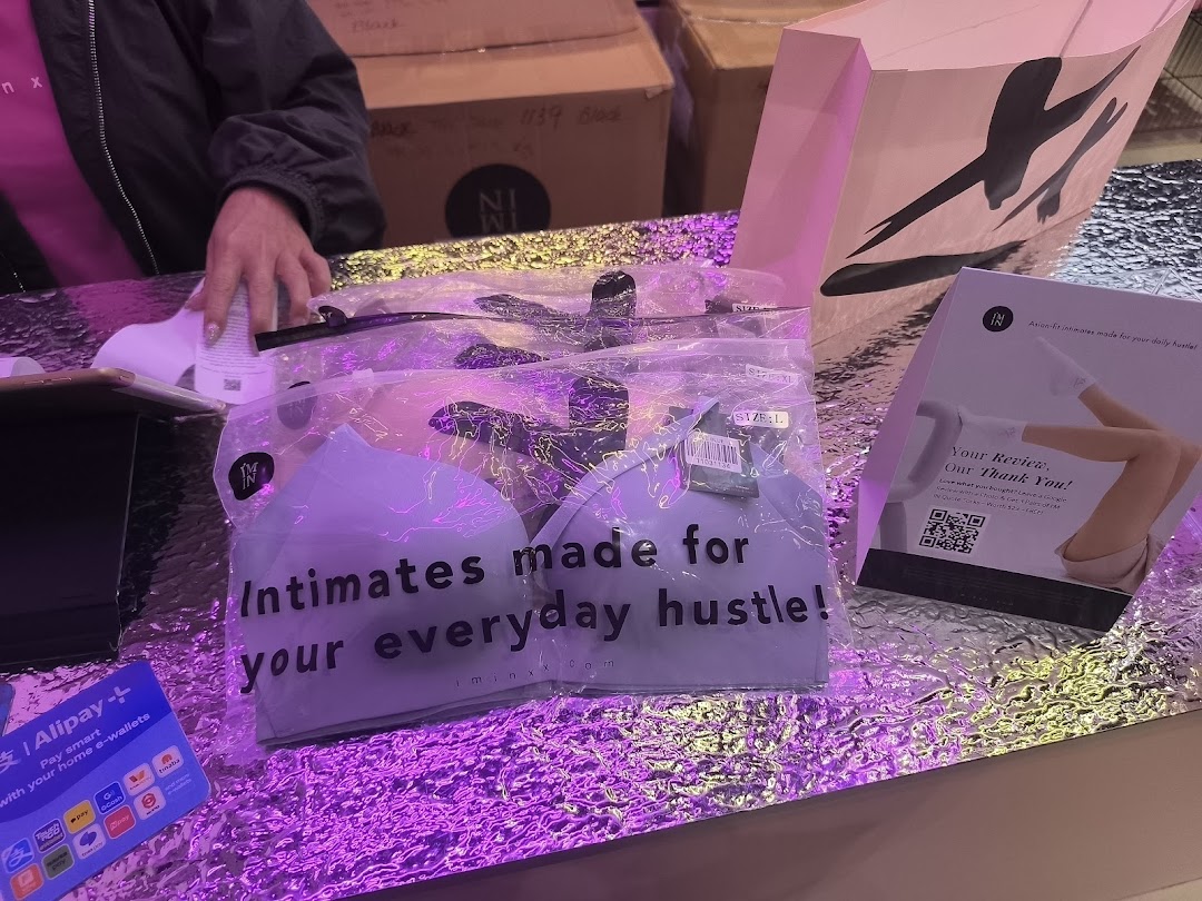 Packaged intimates from IM IN IMINXX displayed on a counter with promotional materials and a shopping bag.