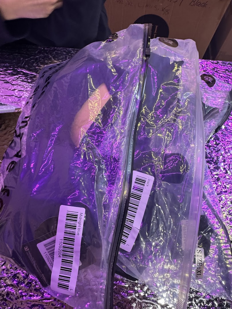 Close-up of packaged clothing items with labels, illuminated by purple light.
