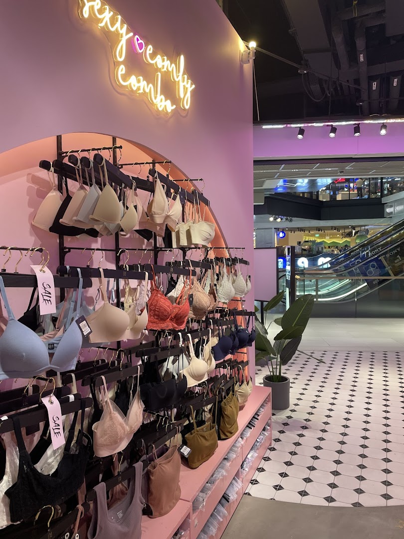 Interior view of IM IN IMINXX, a lingerie shop, showcasing bras on pink displays with a neon sign.