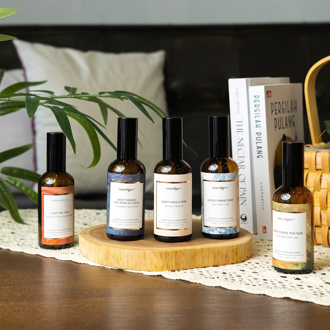 Five bottles of Innerfyre Co. essential oil room spray displayed on a wooden stand and table.