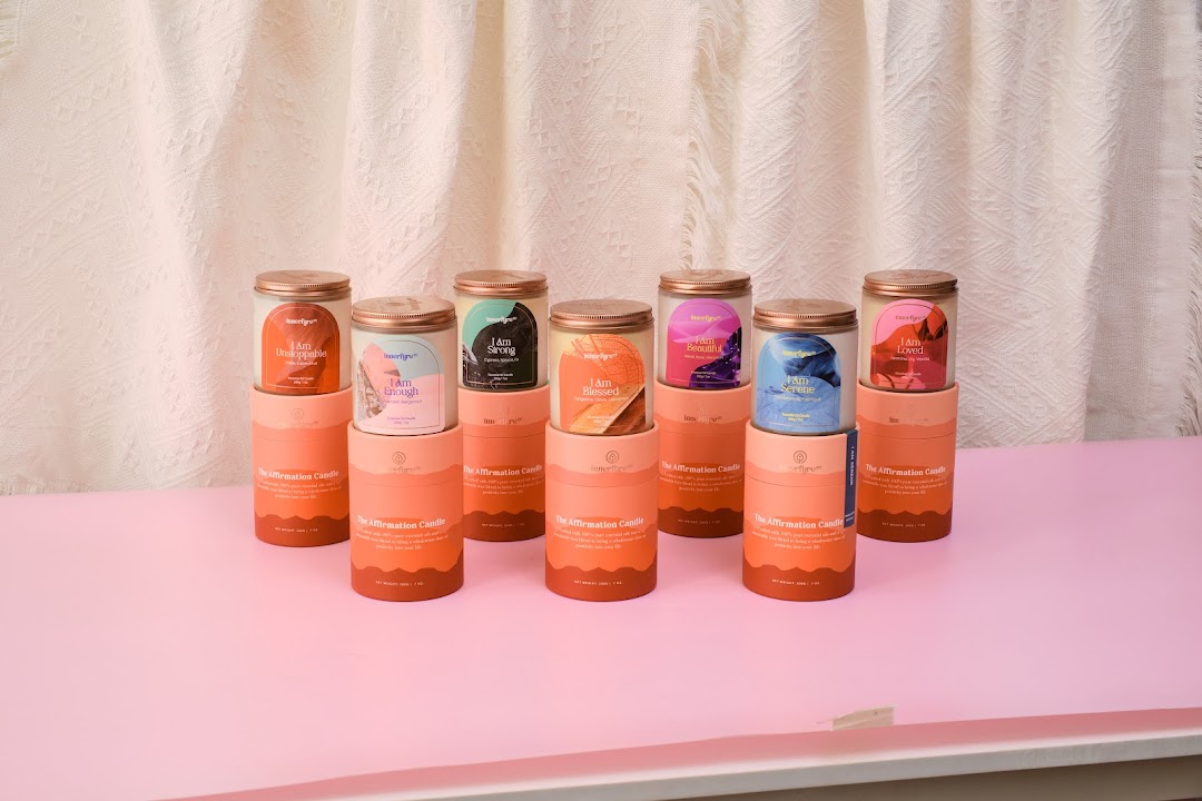 A collection of Innerfyre Co's 'The Affirmation Candle' series displayed on a pink surface.