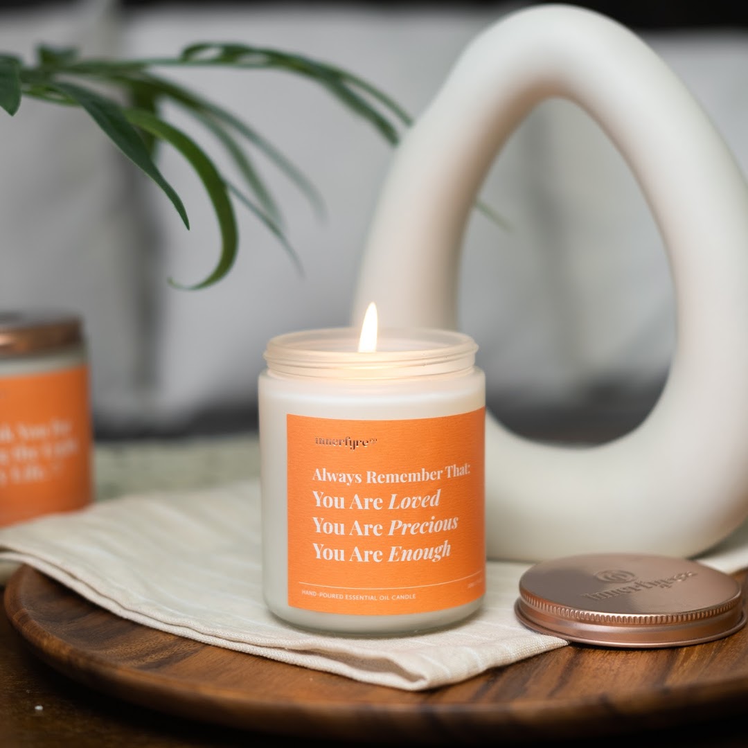 A lit Innerfyre Co. candle with an uplifting message on a wooden tray.