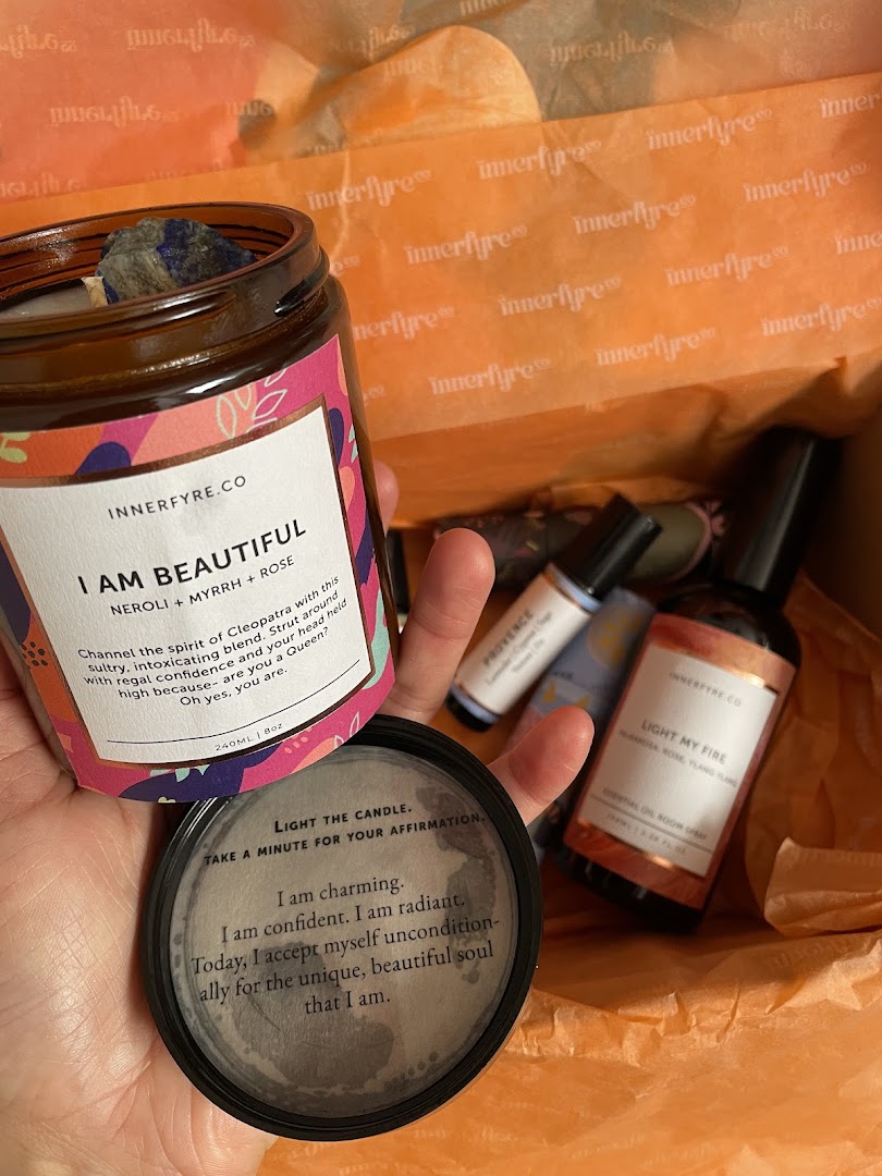 A hand holds an "I Am Beautiful" candle from Innerfyre Co, with other wellness products in a branded box.