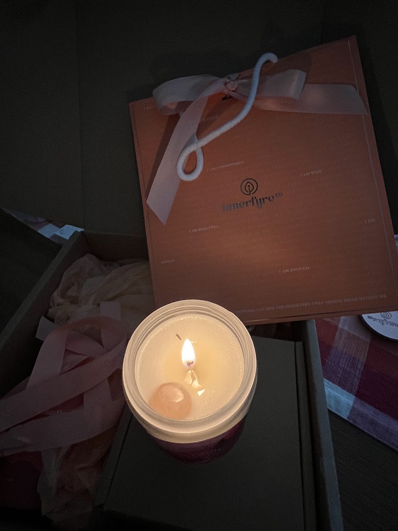 A lit Innerfyre Co. candle with a crystal, alongside a branded gift box, showcasing a product experience.