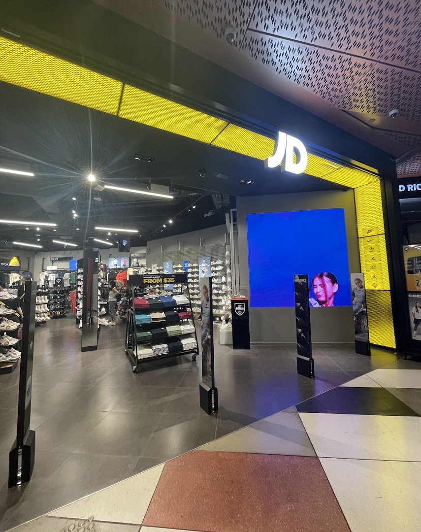 Brightly lit entrance of JD Sports, showcasing sportswear, footwear, and a large digital display.