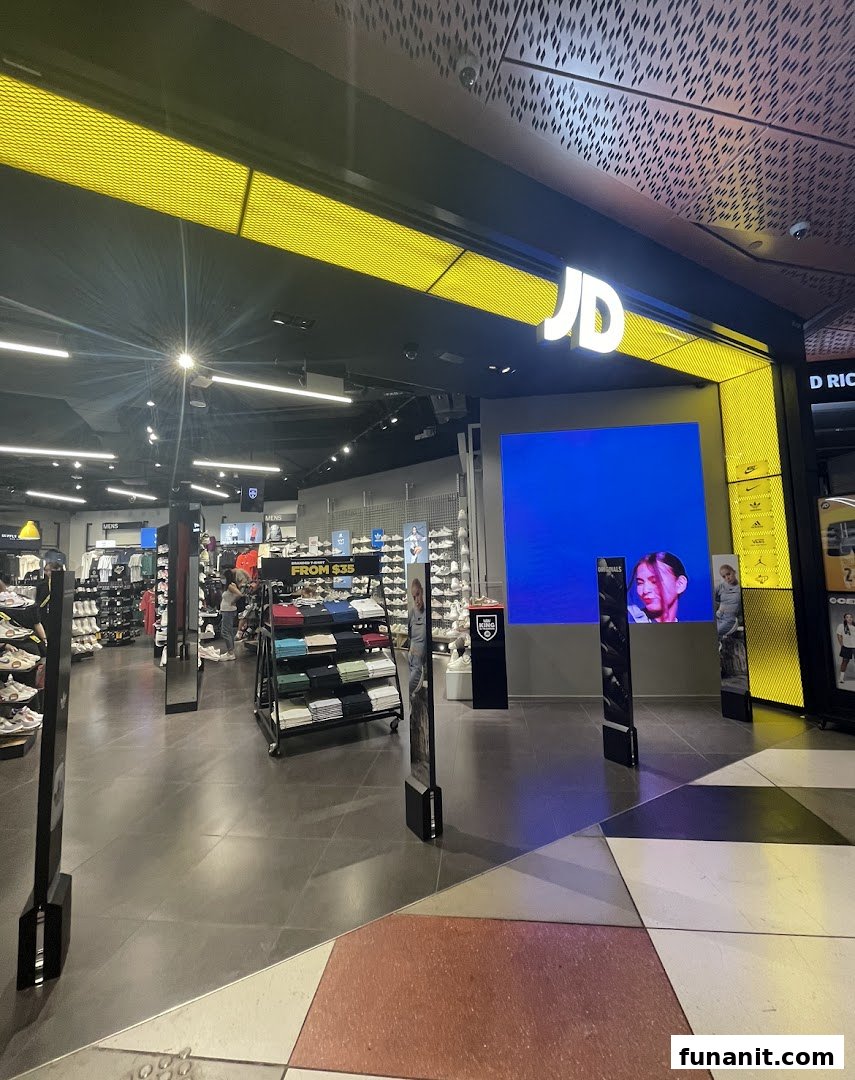 Brightly lit entrance of JD Sports, showcasing sportswear, footwear, and a large digital display.