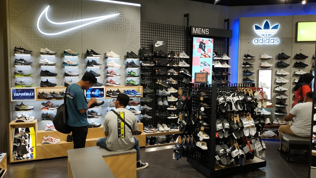 Customers browse a wide selection of sneakers and sandals in a brightly lit JD Sports store.