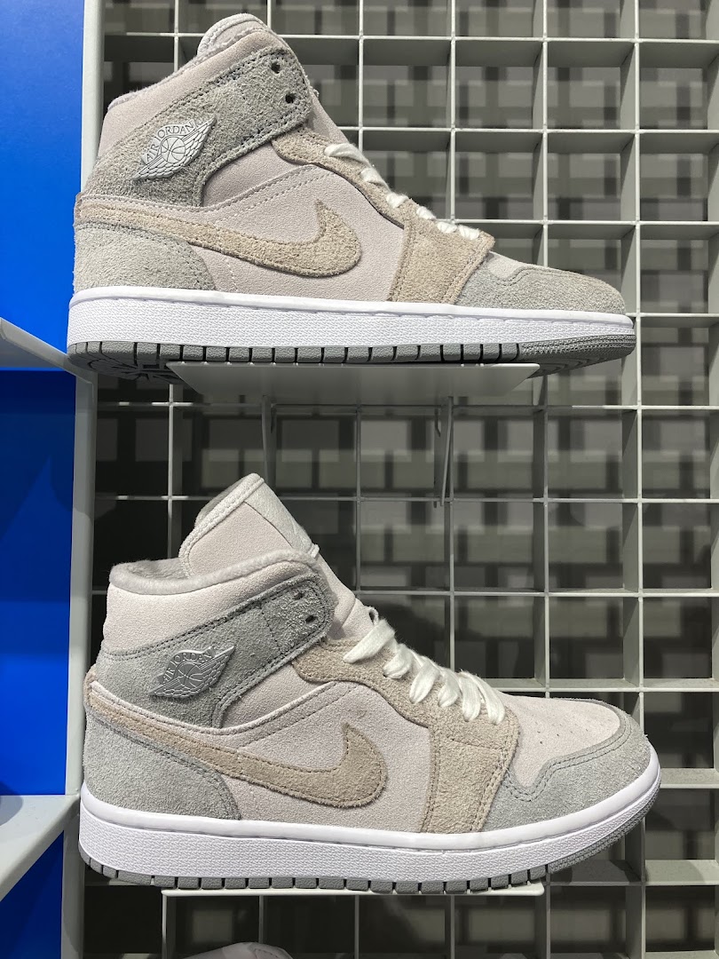 Two pairs of stylish grey and beige sneakers are displayed on a grid shelf.