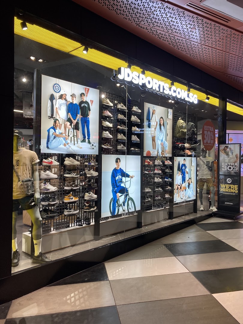 The brightly lit storefront of JD Sports, showcasing athletic footwear, apparel, and mannequins in display windows.