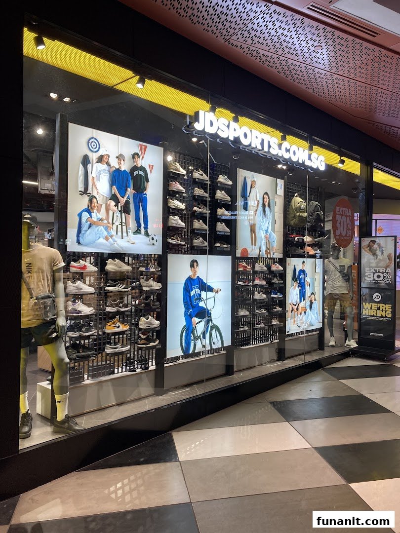 The brightly lit storefront of JD Sports, showcasing athletic footwear, apparel, and mannequins in display windows.