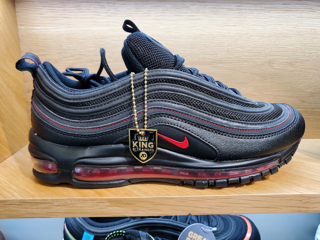 A black and red Nike Air Max 97 sneaker with a JD Sports tag displayed on a wooden shelf.