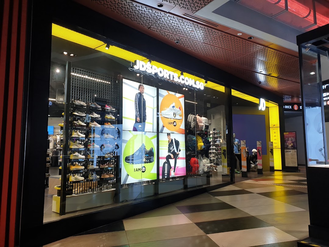 The brightly lit storefront of JD Sports, showcasing athletic footwear displays and digital screens.