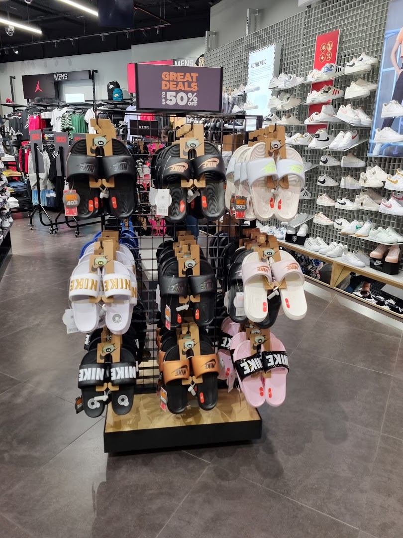 An interior view of JD Sports showcasing a display of Nike sandals and a wall of sneakers, with a 'Great Deals' sign.
